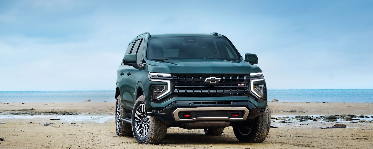 Vista frontal de la Chevrolet Tahoe 2025 Z71 en color verde sobre la arena, con diseño robusto y luces LED encendidas