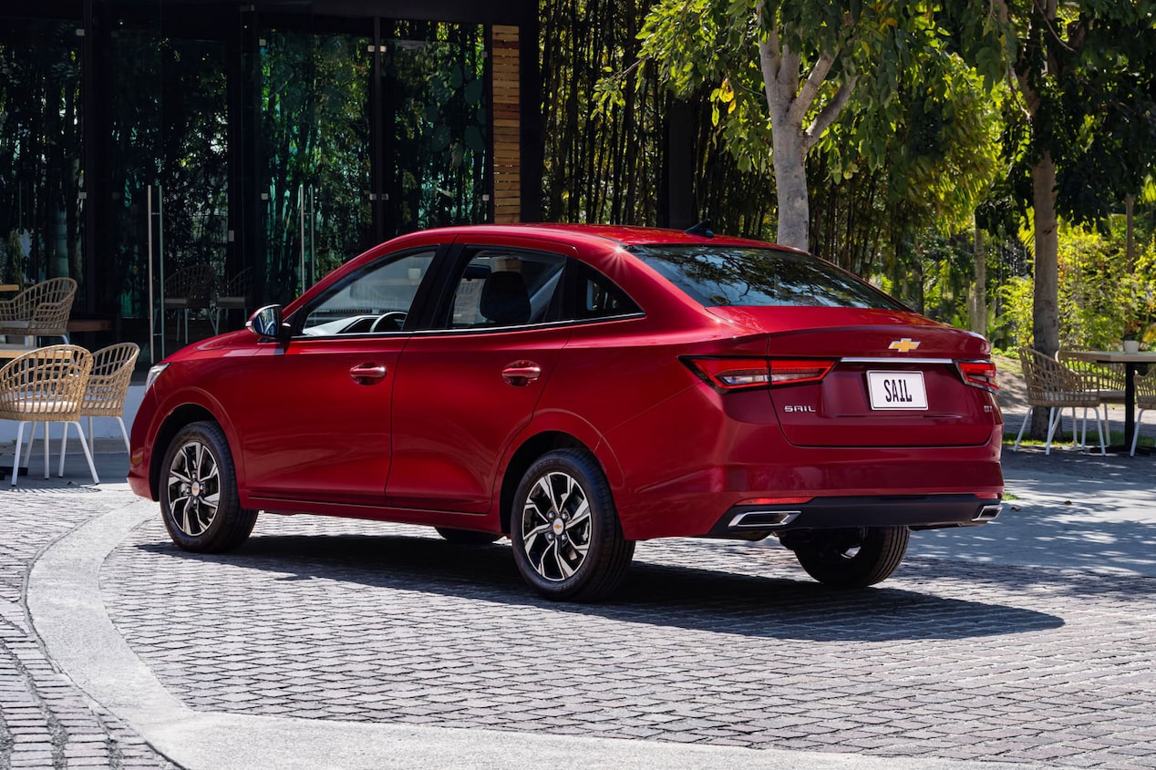 Vista trasera de la Chevrolet Sail Sedan estacionada, con árcoles, meses y sillas al fondo.