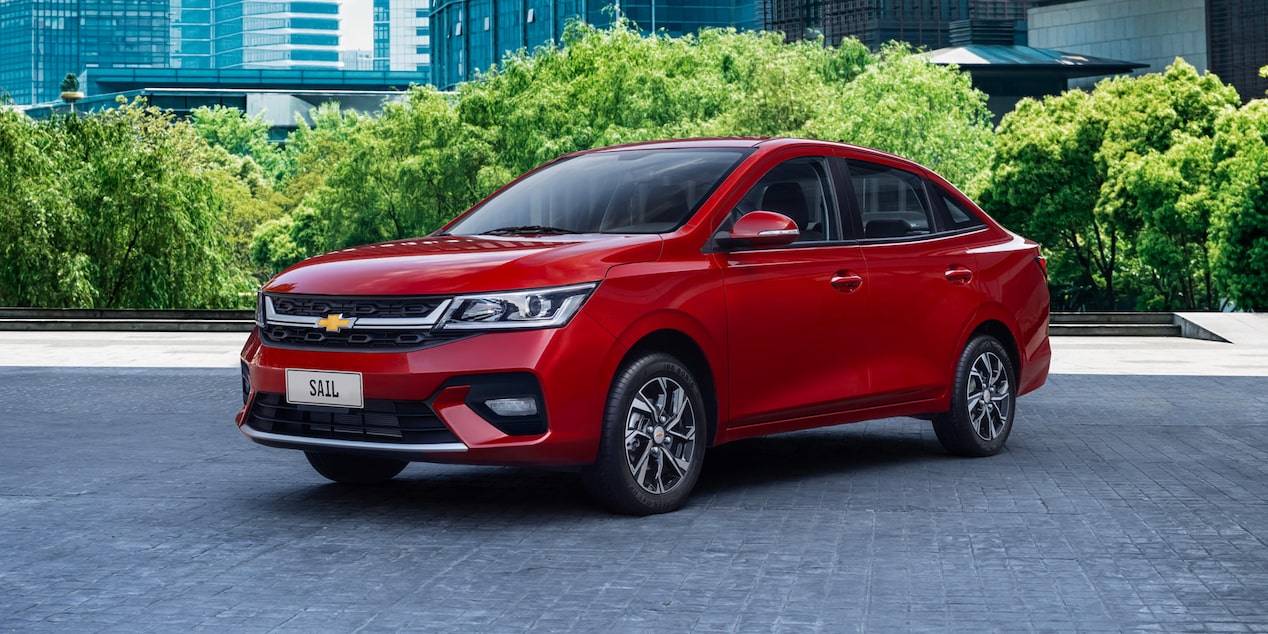 Chevrolet Sail Sedán estacionado en una zona urbana con arboles de fondo.