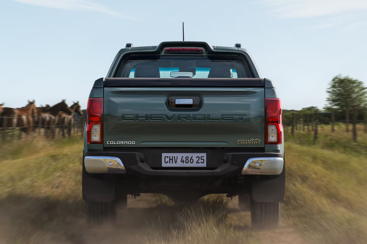 Vista trasera de una Chevrolet Colorado circulando por una calle de tierra en el campo, con caballos y árboles de fondo.