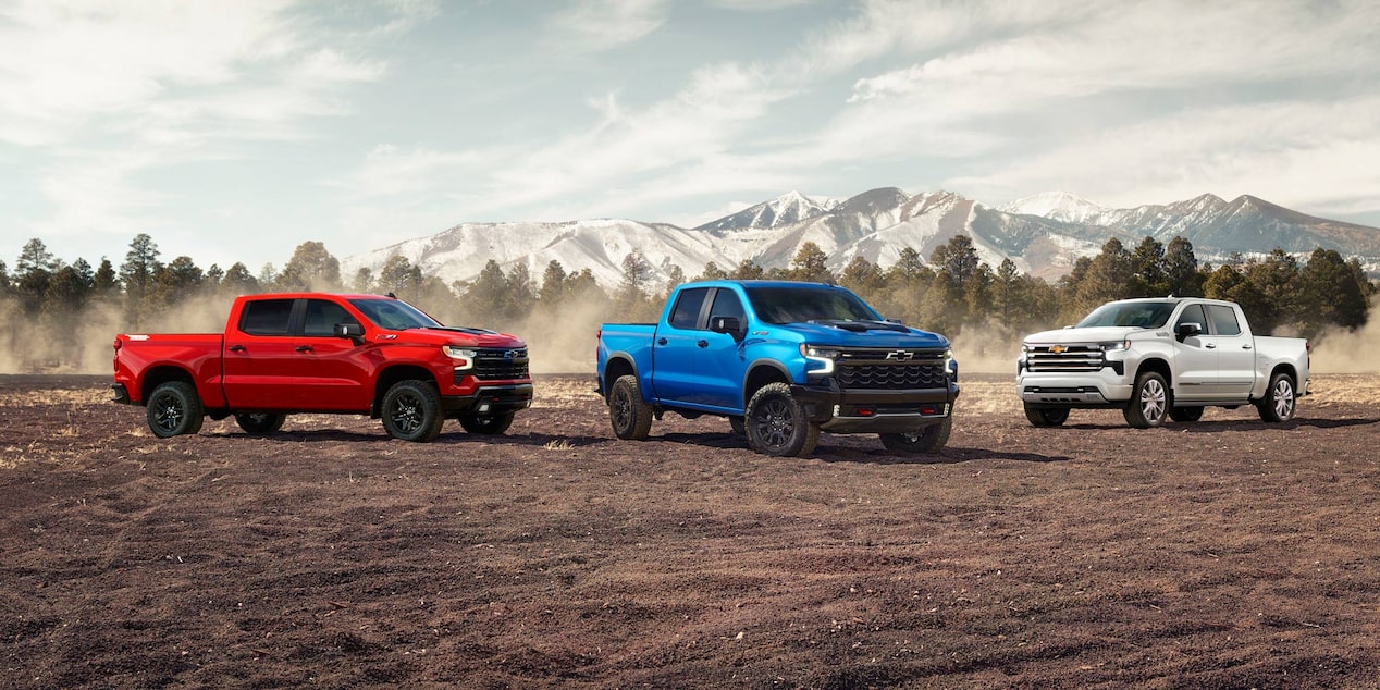 Los tres modelos de la Chevrolet Silverado estacionadas en el campo con montañas de fondo.